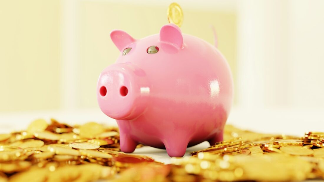 Cofrinho rosa cercado por uma pilha de moedas douradas