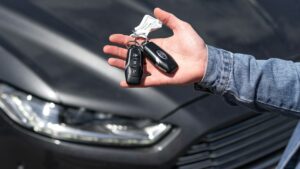 Mão segurando a chave de um carro em frente ao veículo Mão segurando a chave de um carro em frente ao veículo